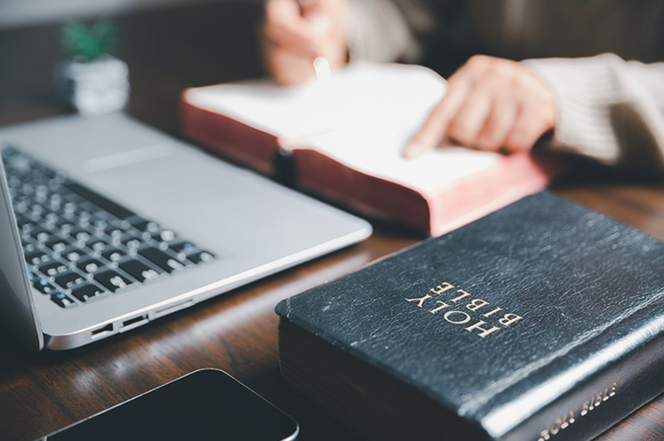 Sermon preparation workspace with Holy Bible, laptop, and study materials on wooden desk